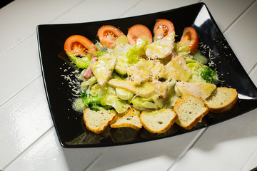 Caesar salad with bacon and quail eggs Black plate on a white wooden