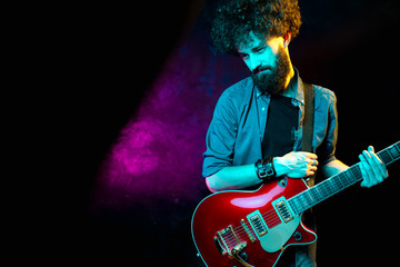 Obraz premium Close-up photo of hipster man with red guitar in neon lights. Rock musician is playing electrical guitar.
