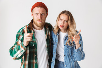Angry serious young loving couple posing isolated over white wall background gesturing with finger.