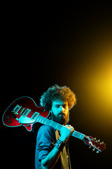 Portrait of hipster man with curly hair with red guitar in neon lights.