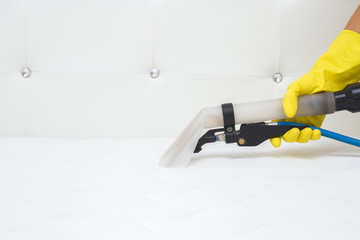 Employee hand in yellow protective glove cleaning modern white mattress with professionally...