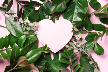Tropical nature background with green leaves and pink heart shaped paper for copy space. Top view. Flat lay. Creative advertising. Summer and love concept.