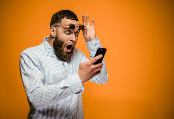 Shocked hipster man hold on eye glasses and looking at the phone. emotional male can't believe in...