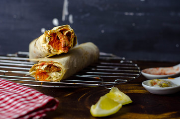 Shaurma, burrito, chicken roll in a pita with fresh vegetables and cream sauce on dark wooden background.