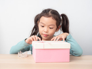 Little cute girl and the gift box on wooden table and white background. Kid excited to receive gifts.