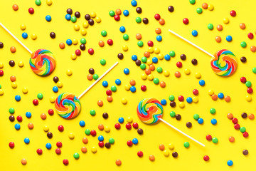 Multicolored lollipop, rainbow colorful candies on yellow background. Coated chocolate sweet pieces texture. Top view. Flat lay. Confetti for holidays, birthday party concept