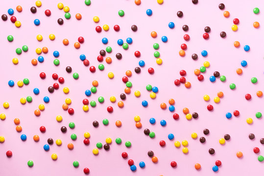 Rainbow colorful candies on pink background. Coated chocolate sweet pieces texture. Top view. Flat lay. Confetti for holidays, birthday party concept