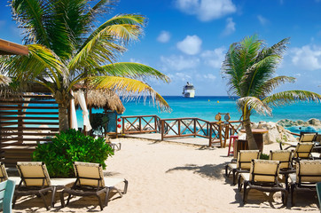Beach at tropical resort with cruise ship sailing to port in distance