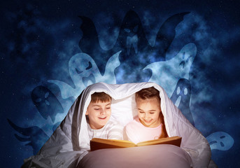 Happy little kids reading book in bed
