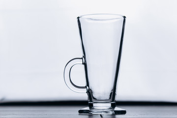 empty transparent glass cup on a gray silver background close-up. high cup with handle and leg. copy space, texture, background