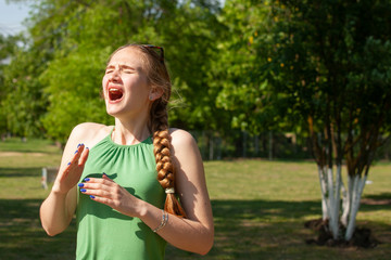 Young woman with allergy during sunny day is wiping her nose.