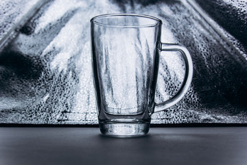 empty transparent glass cup on a gray silver background close-up. high cup with handle and leg. copy space, texture, background