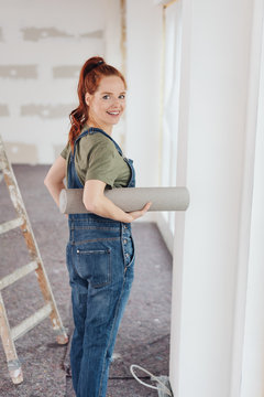 Happy young woman carrying a roll of wallpaper