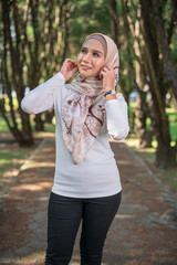 Portrait young attractive Asian Muslim woman, smile and happy face, at green park. New modern, contemporary casual fashion in hijab, classic and vintage summer warm look. Copy space for advertising.