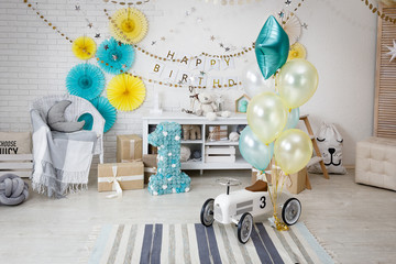 Birthday decorations with gifts, toys, garlands and figure for little baby party on a white bricks background. 