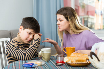 Obraz na płótnie Canvas Upset mother and unhappy son arguing during breakfast indoors