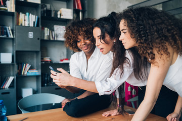 three multiracial young friends looking the smartphone in modern office