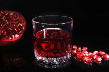 Glass with pomegranate juice Pomegranate seeds and Beautiful ripe pomegranate on black mirror background with place for copy space.