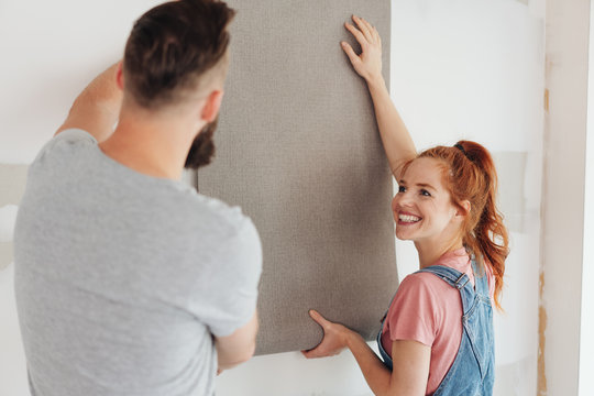 Happy young woman holding up a roll of wall paper