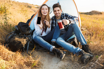 Naklejka na ściany i meble Happy young loving couple outside in free alternative vacation camping drinking hot tea.