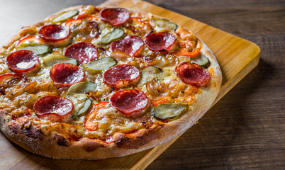 Pepperoni Pizza with Mozzarella cheese, salami, bacon, Tomato sauce, pepper, Spices and pickled cucumbers. Italian pizza on wooden table background