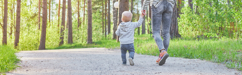 mother and child walk by the handle in the park in sunny summer weather. back view.