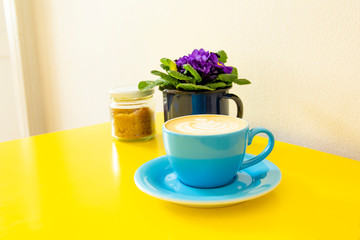 hot cappucino in blue cup on yellow table with purple violet background
