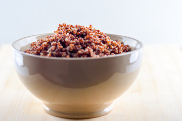Cooked prep red quinoa in a bowl on a wooden background.