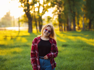 Smiling Blonde in stylish sunglasses and red shirt portrait at sunset in the Park