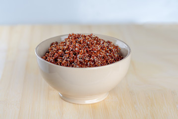 Cooked prep red quinoa in a bowl on a wooden background.