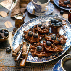 Homemade yummy chocolate waffles on vintage plates with blue ornament stands on wooden dark table