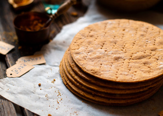 Homemade stack of baked layers of Russian traditional honey cake on baking paper on wooden rustic table 