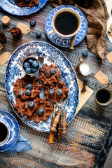 Overhead shot of homemade yummy chocolate waffles on vintage plates with blue ornament stands on wooden dark table