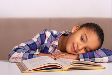 The schoolgirl sits at the table at home and does his homework.