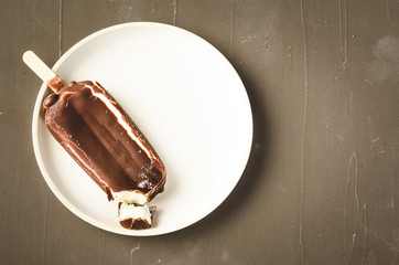 ice cream. Homemade dark chocolate ice cream on a stick in white bowl. Top view, dark background. Sweet dessert closeup, wide angle