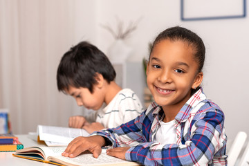 The schoolgirl and schoolboy sit at the table  indoors and do their homework