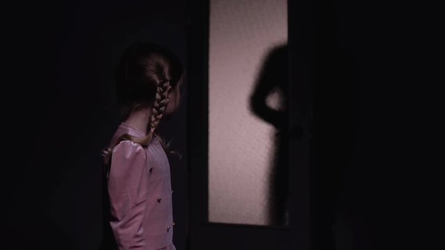Little girl afraid of dark male silhouette opening room door, horror nightmare