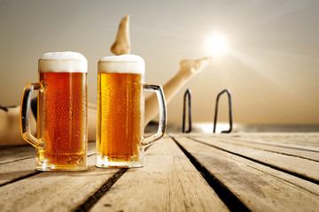 Cold beer on wooden pier and summer sunset time. Slim young woman legs and free space for your decoration. 