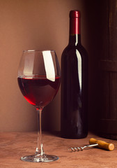 A glass of red wine and a bottle on dark background. Copy space. Still life style dark. Selective focus. Vertical frame.