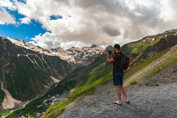 Naklejka premium Tourist with backpack stands on top of plateau and photographs mountains. Caucasus Mountains, Gorge Baksan