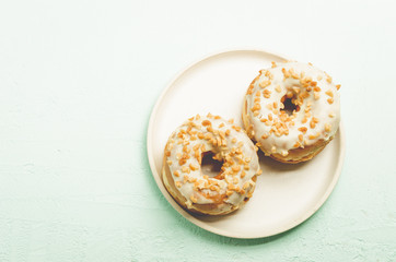 Donat. A plate from donata in white glaze with nuts. Top view and copy space. Fresh pastries. Sweet food concept.