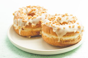 Donat. A plate from donata in white glaze with nuts. Fresh pastries. Sweet food concept.