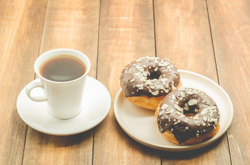 Сoffee break. White cup with black coffee and donat in chocolate glaze. Wooden background.