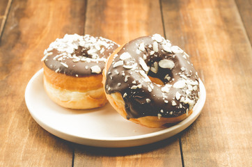 Donat. Donat in chocolate is strewed with grated almonds. Closeup. Donat in a white bowl on a wooden background.