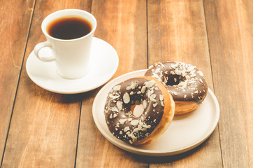 Сoffee break. White cup with black coffee and donat in chocolate glaze. Wooden background.
