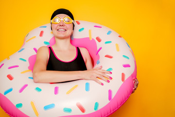 Image of happy woman in swimming goggles, swimsuit with donut life buoy on empty orange background
