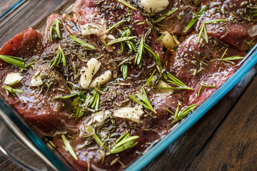 Marinated Raw Tenderloin Meat with Rosemary, Garlic and Olive Oil in Glass Bowl Ready to Cook.