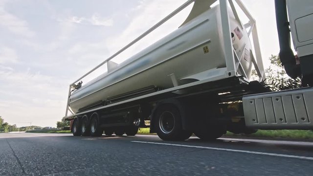 Cargo truck with fuel diesel cargo trailer driving on a highway. White Truck delivers goods in early hours of the Morning - very low angle drive thru close up shot.