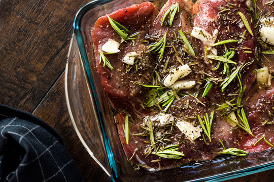 Marinated Raw Tenderloin Meat with Rosemary, Garlic and Olive Oil in Glass Bowl Ready to Cook.