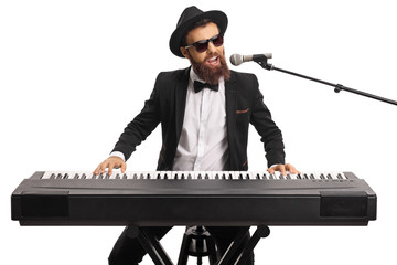 Man with sunglasses and a beard playing a digital piano and singing on a microphone